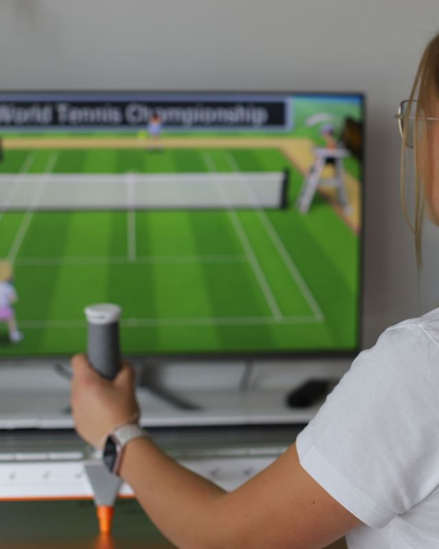 Eine Therapeutin führt den Griff des Smart Board, auf dem Bildschirm läuft ein Tennisspiel