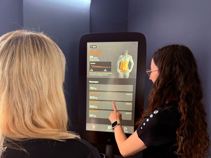 Eine Therapeutin zeigt einer Patientin ihre Auswertung am Bildschirm eines EGYM-Geräts